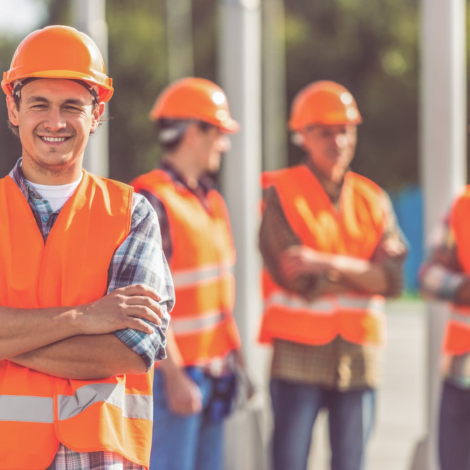 Équipe d'ouvriers BTP en gilets de sécurité orange et casques, sourires, sur chantier en lumière naturelle.